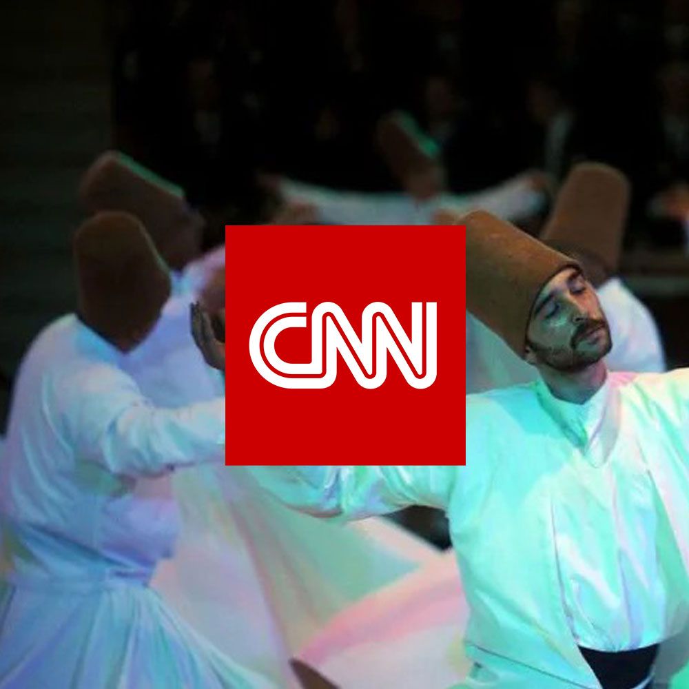 Whirling dervishes in white robes and tall hats perform, CNN logo in the center.