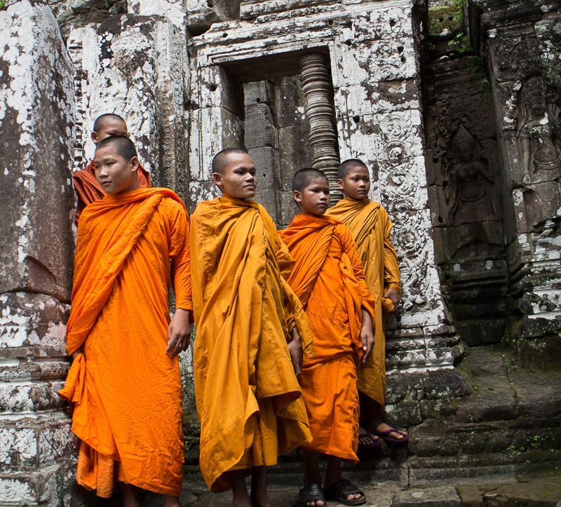 Buddhist monks in orange robes stand before a weathered stone temple entrance.