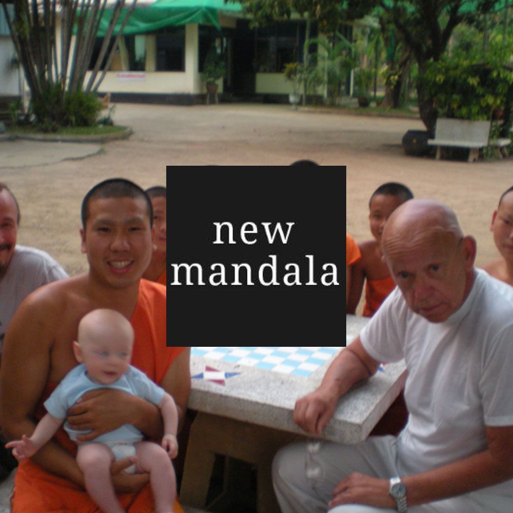 A group of people sitting outside, with a baby, monks, and an older man.