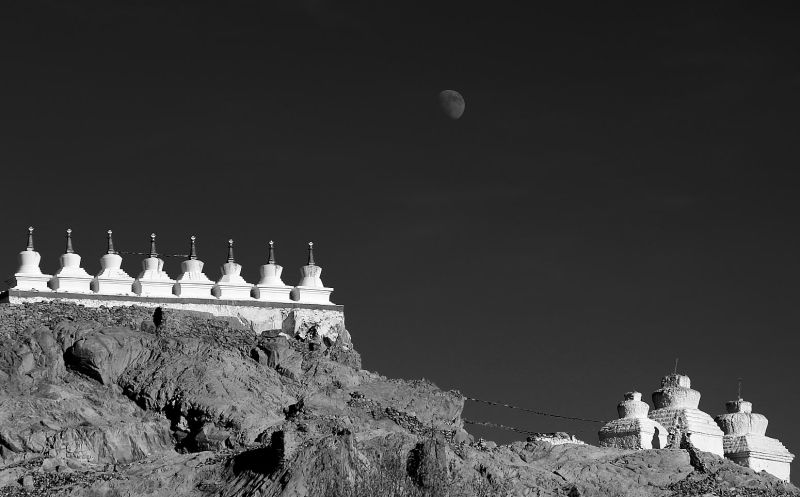 Monochrome photo: Buddhist structures atop a rocky hill under a moonlit sky.