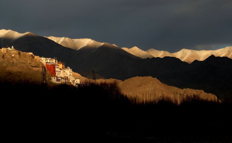 White Buddhist monastery on a hillside at sunset with snow-capped mountains in the background.