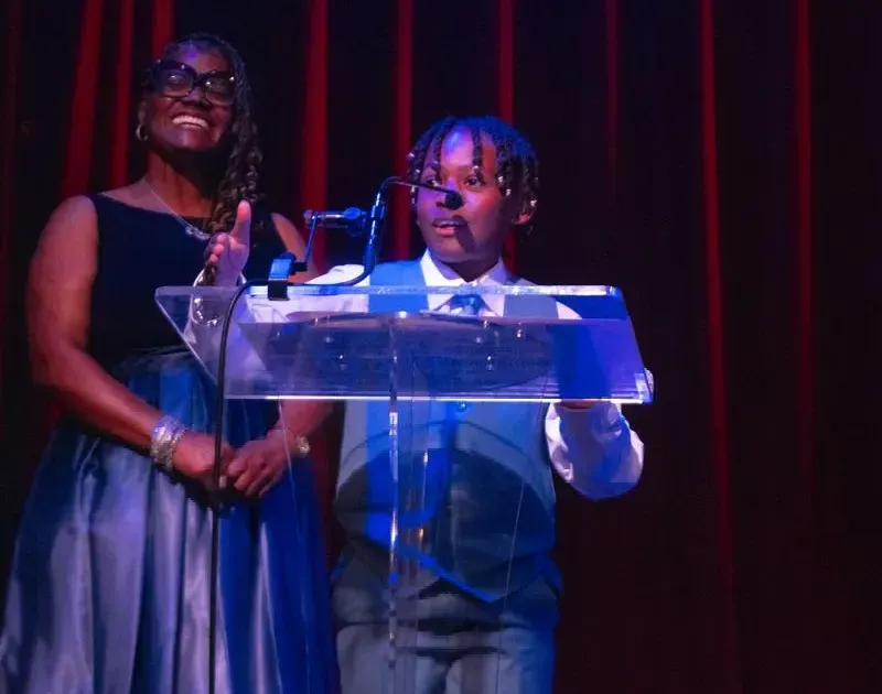 A woman and a boy are standing at a podium in front of a microphone.