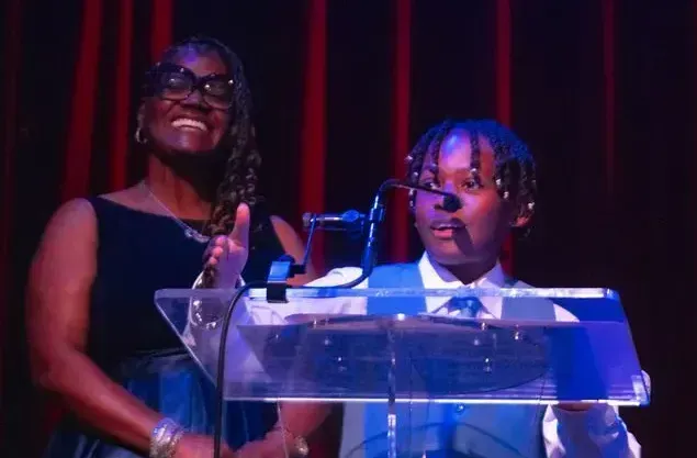 A woman and a boy are standing at a podium with microphones.