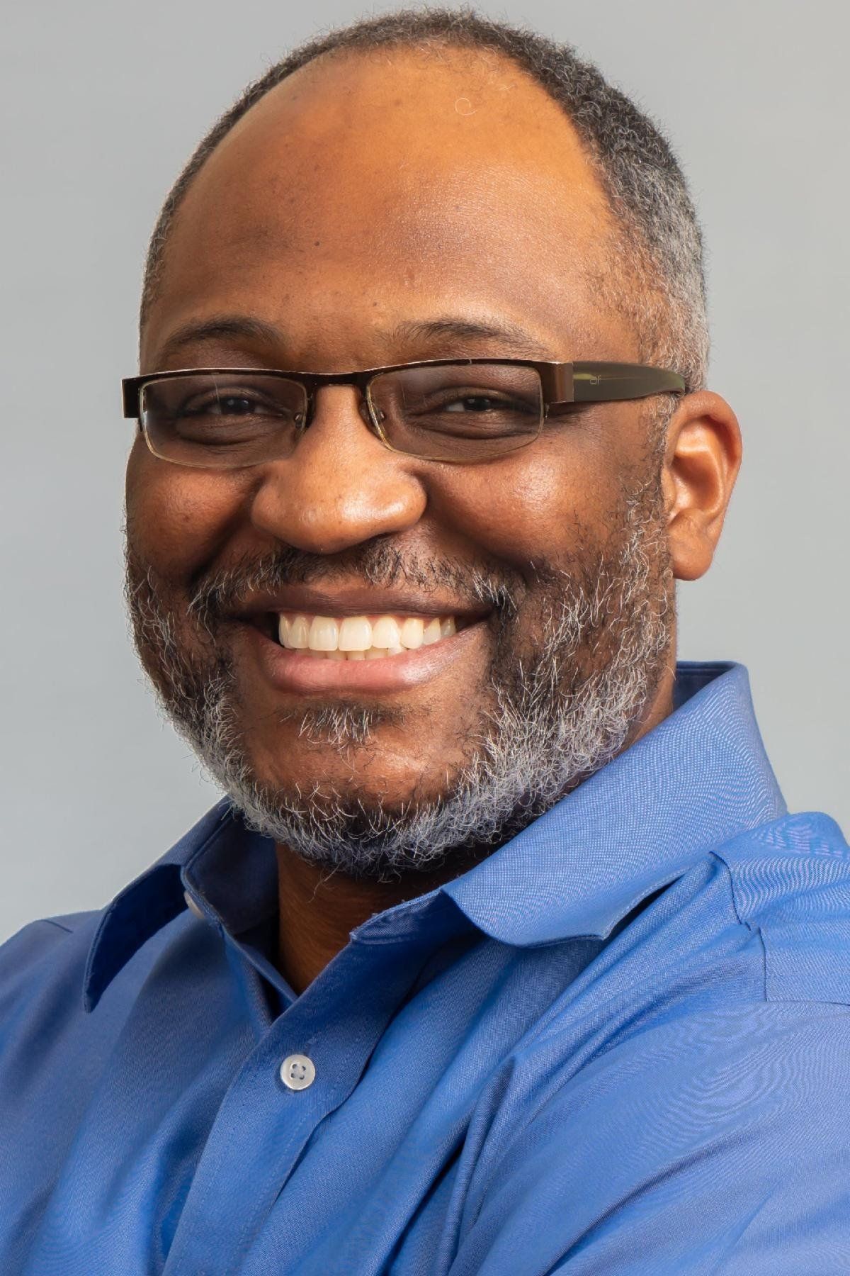 A man wearing glasses and a blue shirt is smiling for the camera.