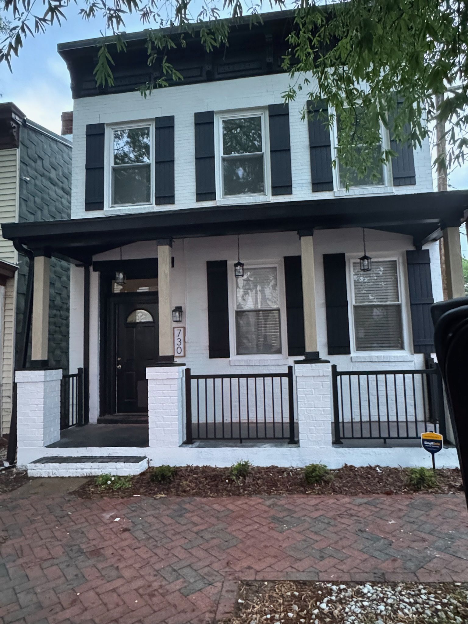Two-story white house with black trim, shutters, and porch. Brick sidewalk in front.