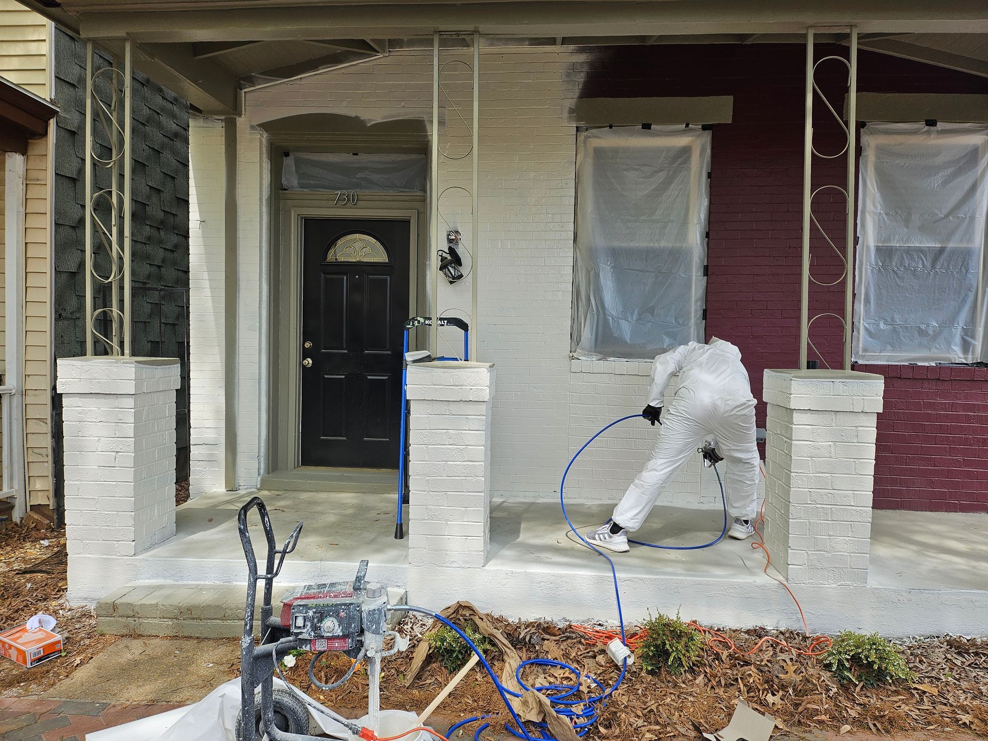 Person in white protective suit sprays paint on a house porch.