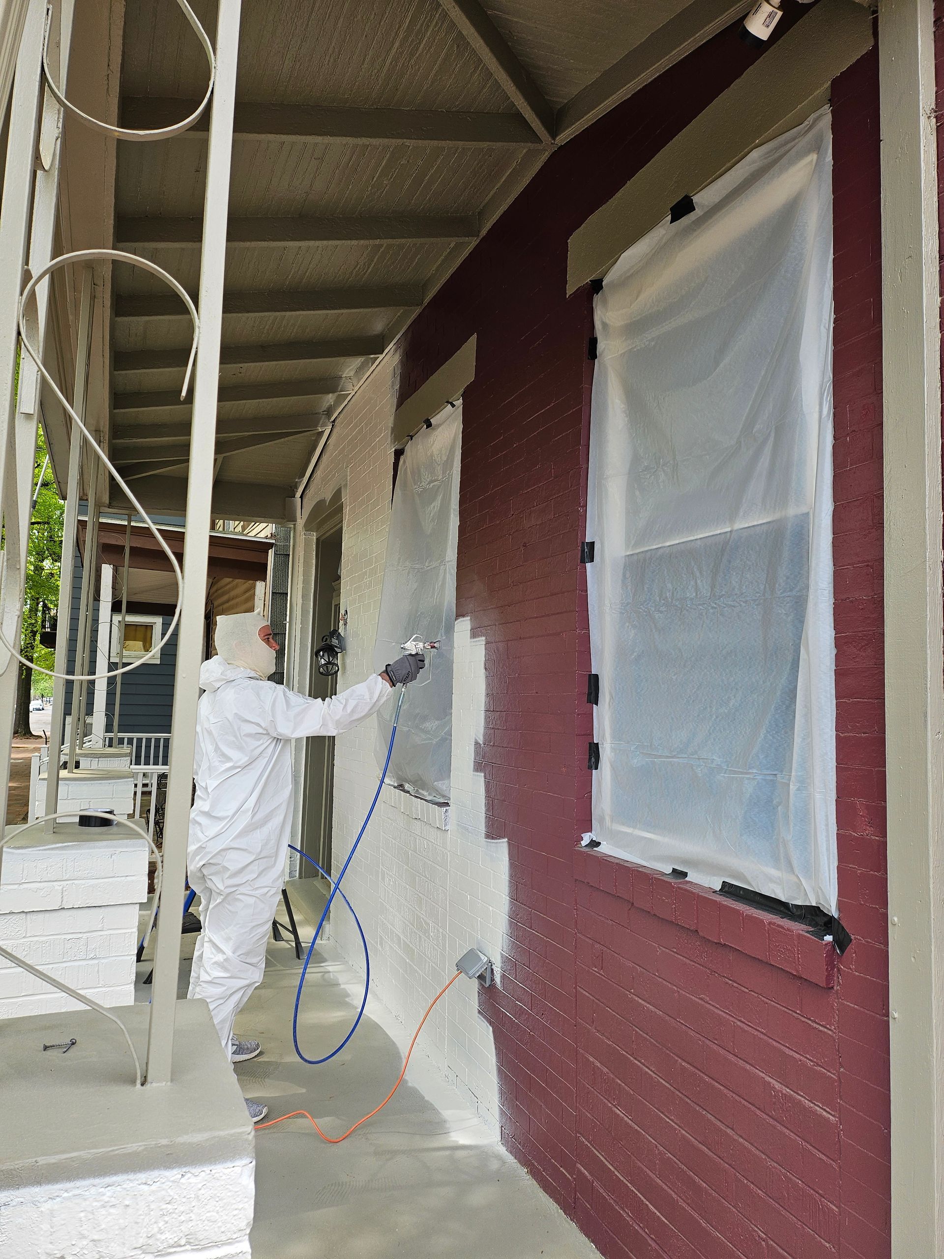Person in protective suit spraying a textured coating on a red brick building exterior.