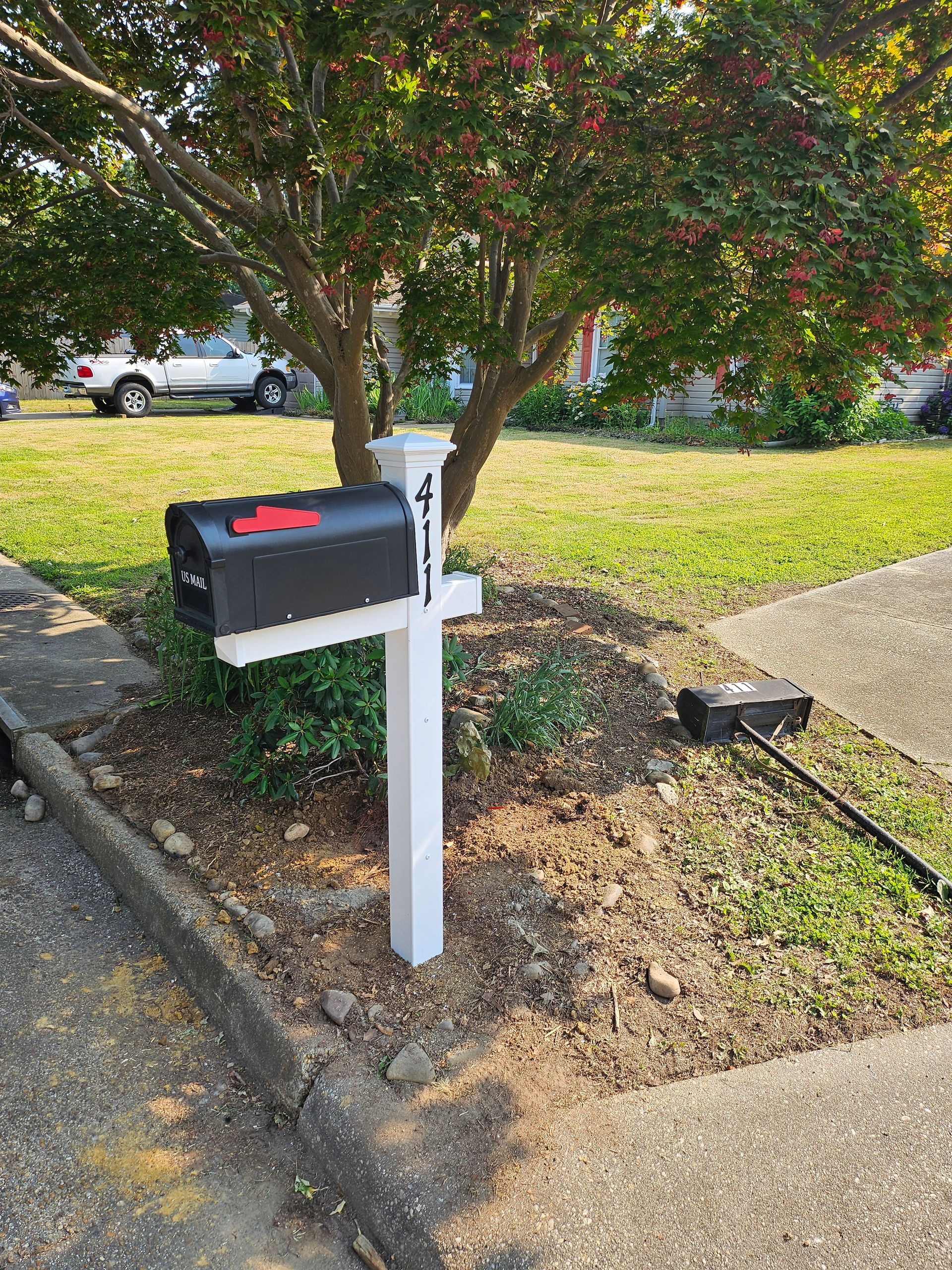 Black mailbox on white post in front yard with a tree.