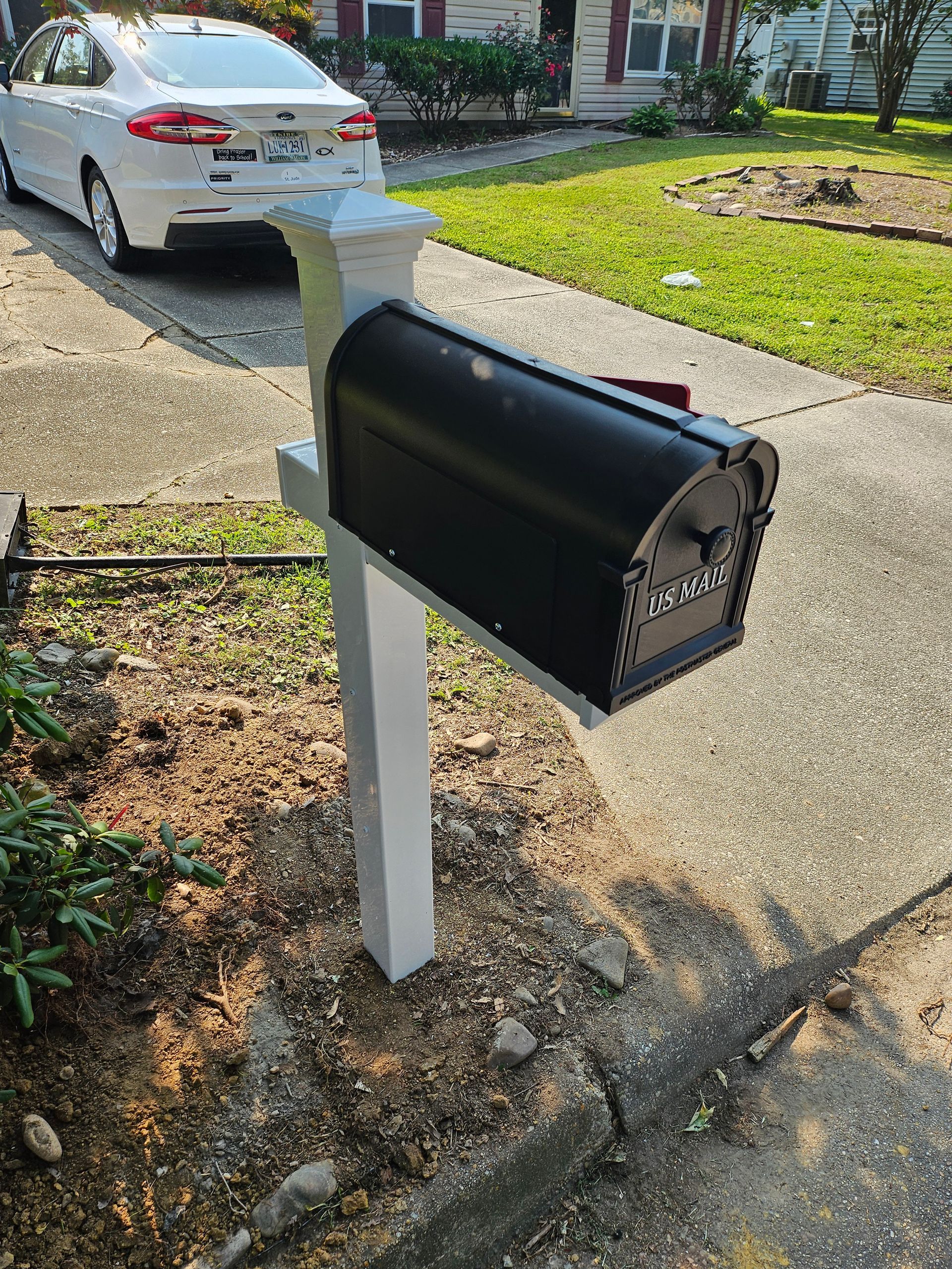 Black mailbox on white post by a driveway.