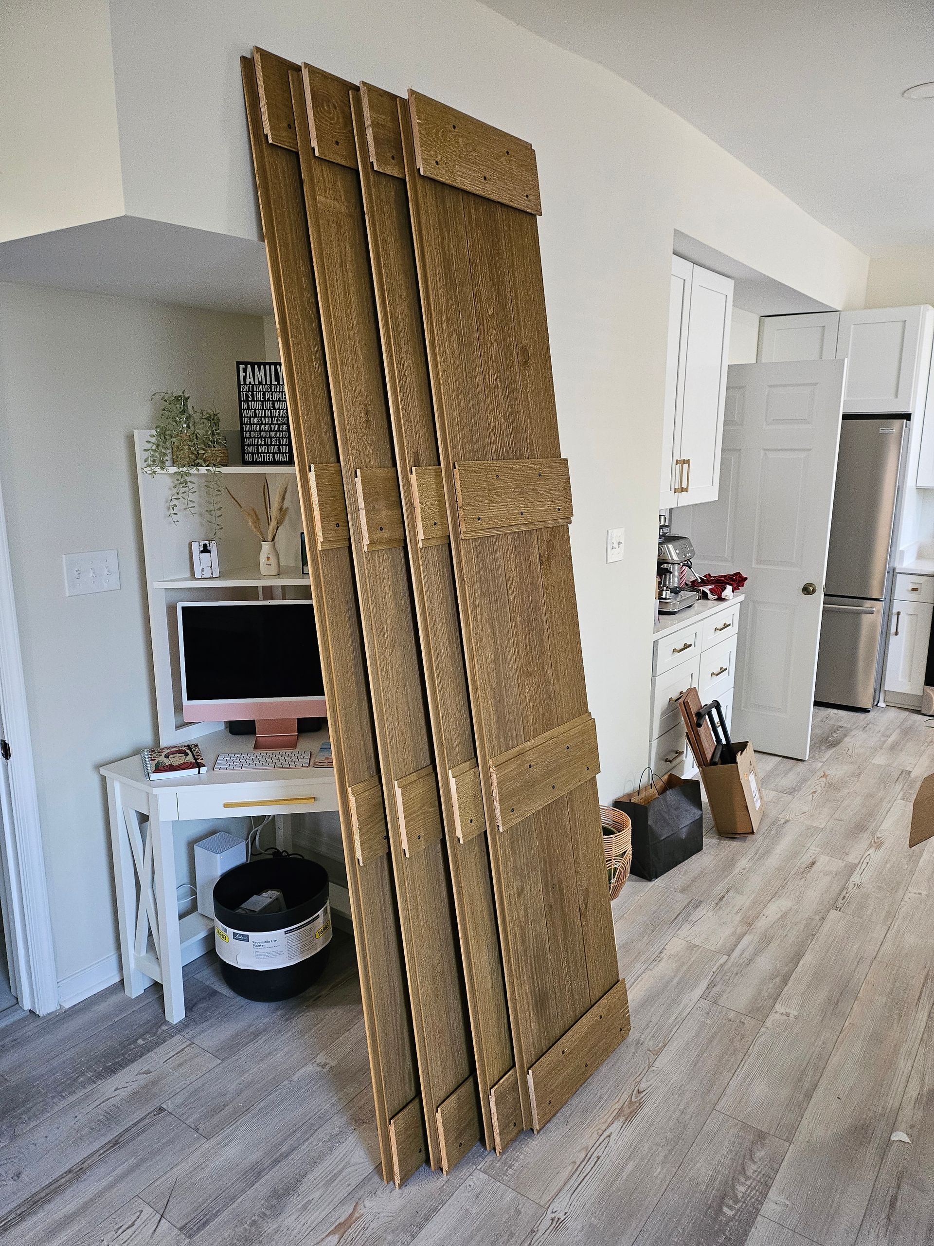 Stack of cardboard panels leaning against a wall in a room with a desk, and kitchen in the background.
