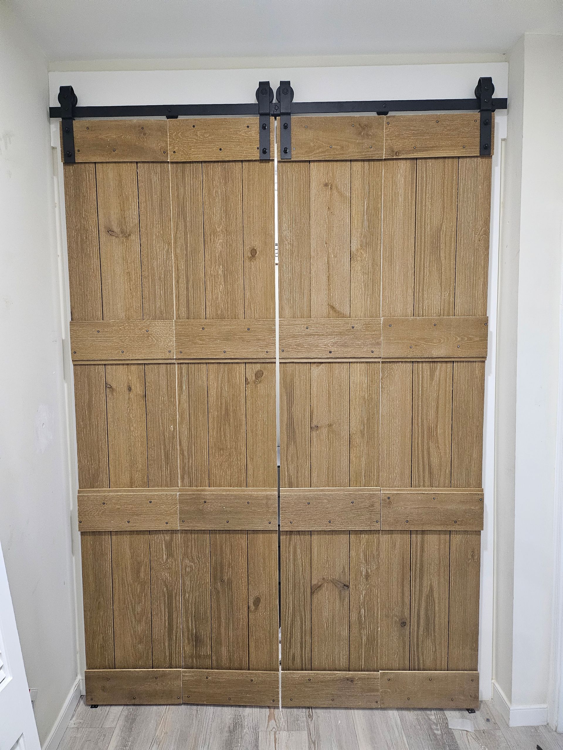 Two wooden barn doors, weathered brown, on black sliding hardware in a white doorway.