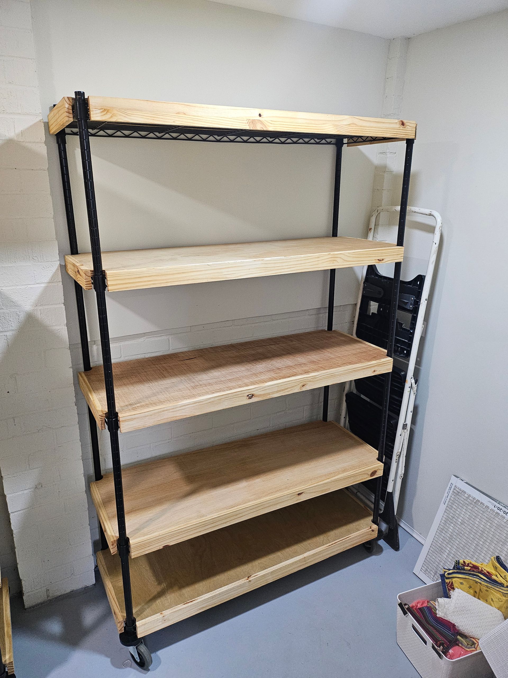 A shelving unit with wooden shelves and black metal frame; in a room with a white wall.