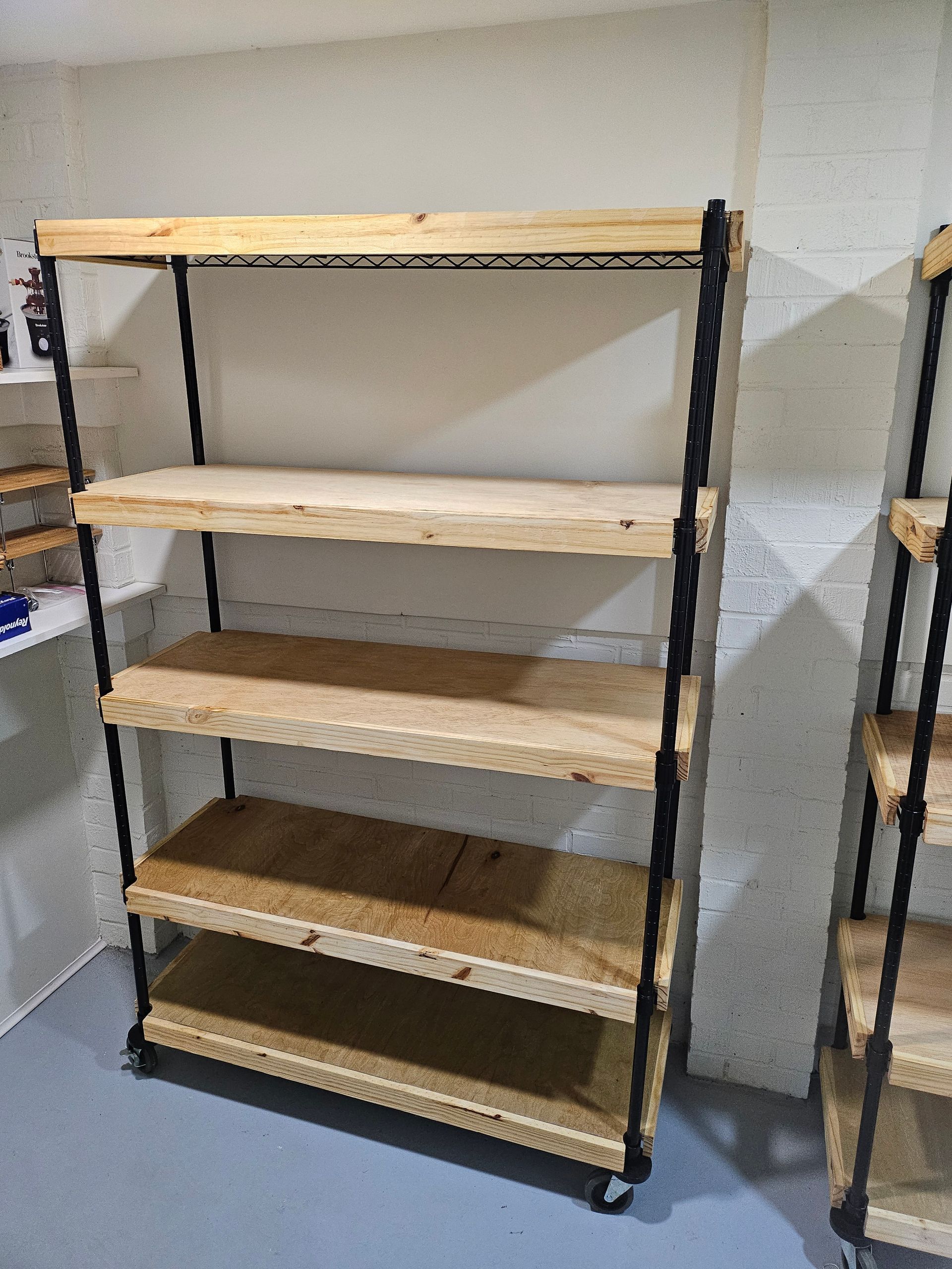 A wooden shelf with five shelves, black frame, set against a concrete wall.