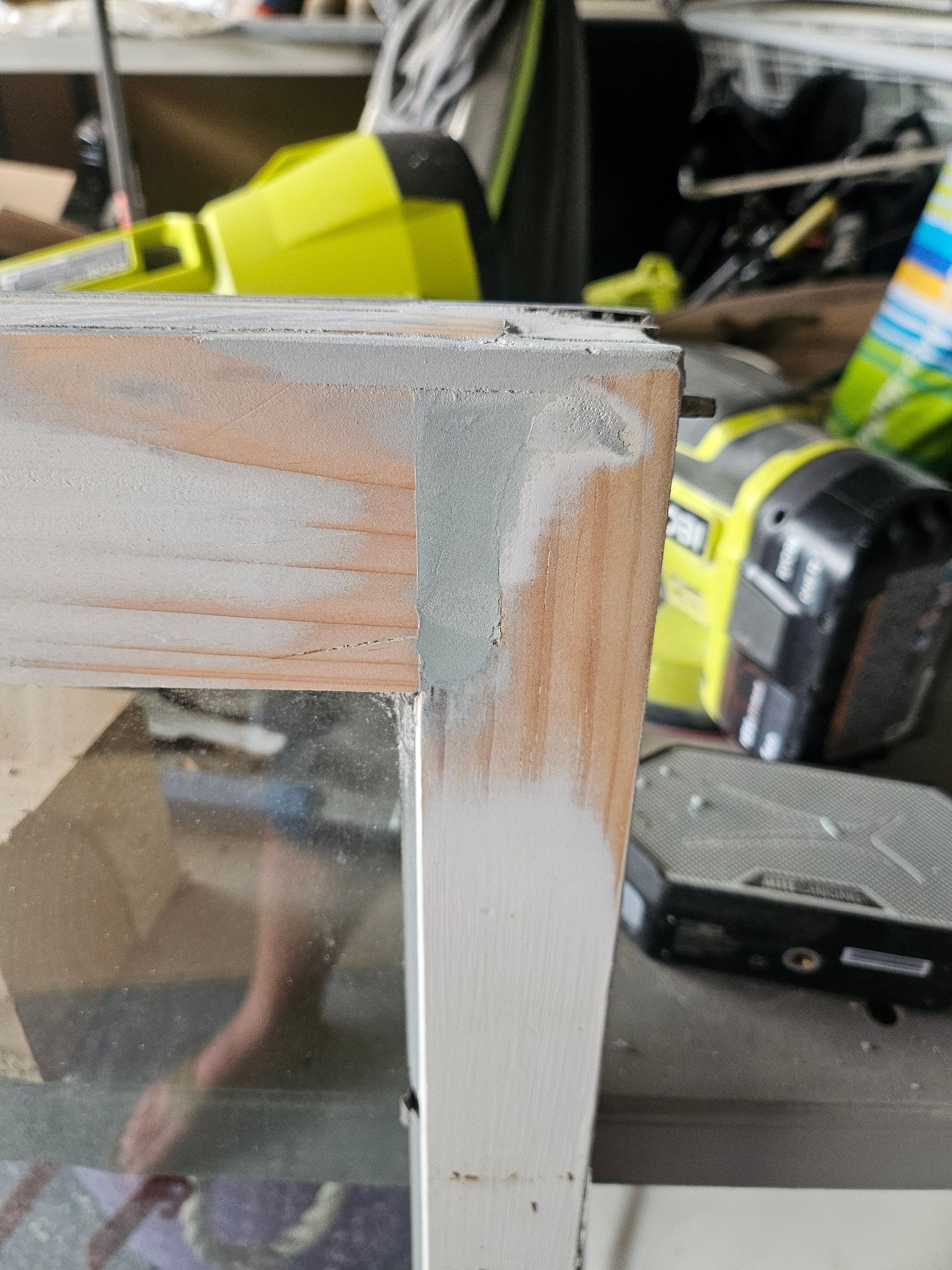 Close-up of a sanded wooden frame corner, showing the grain and a metal edge, with tools in the background.