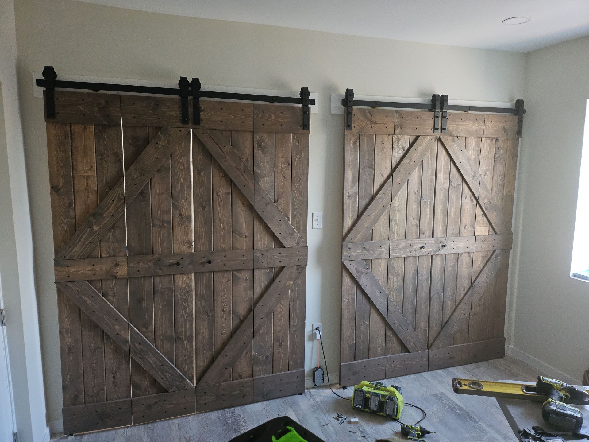 Two rustic wooden barn doors mounted on black sliding tracks, indoors against a light wall.