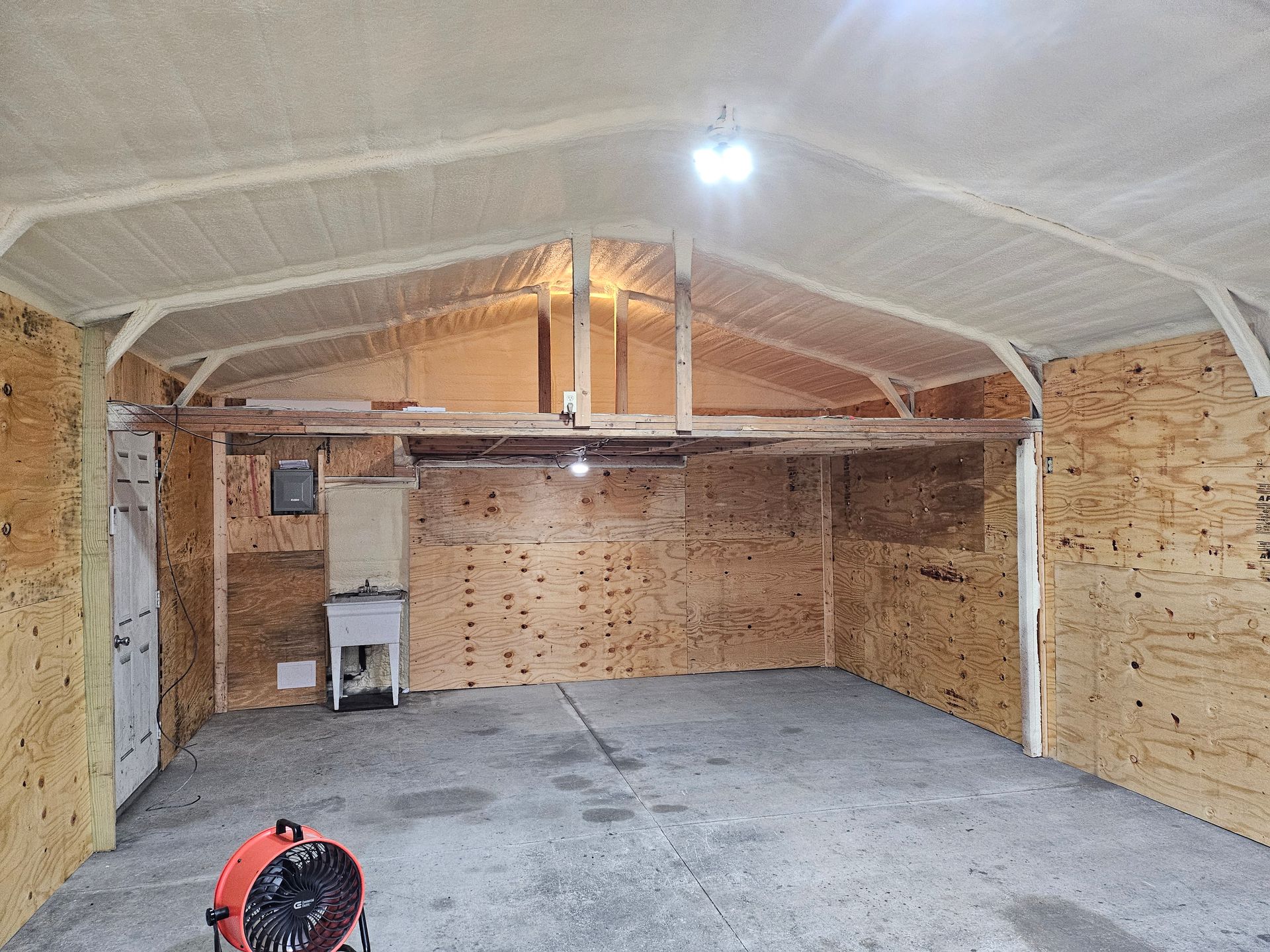 Interior of a garage. Walls and ceiling insulated with spray foam. Concrete floor.