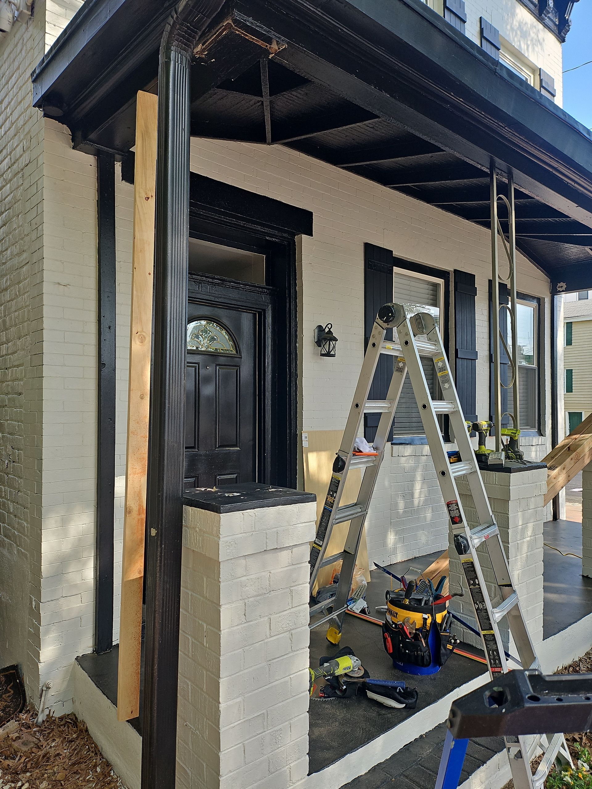 A house porch under construction with a ladder, tools, and black and white paint.