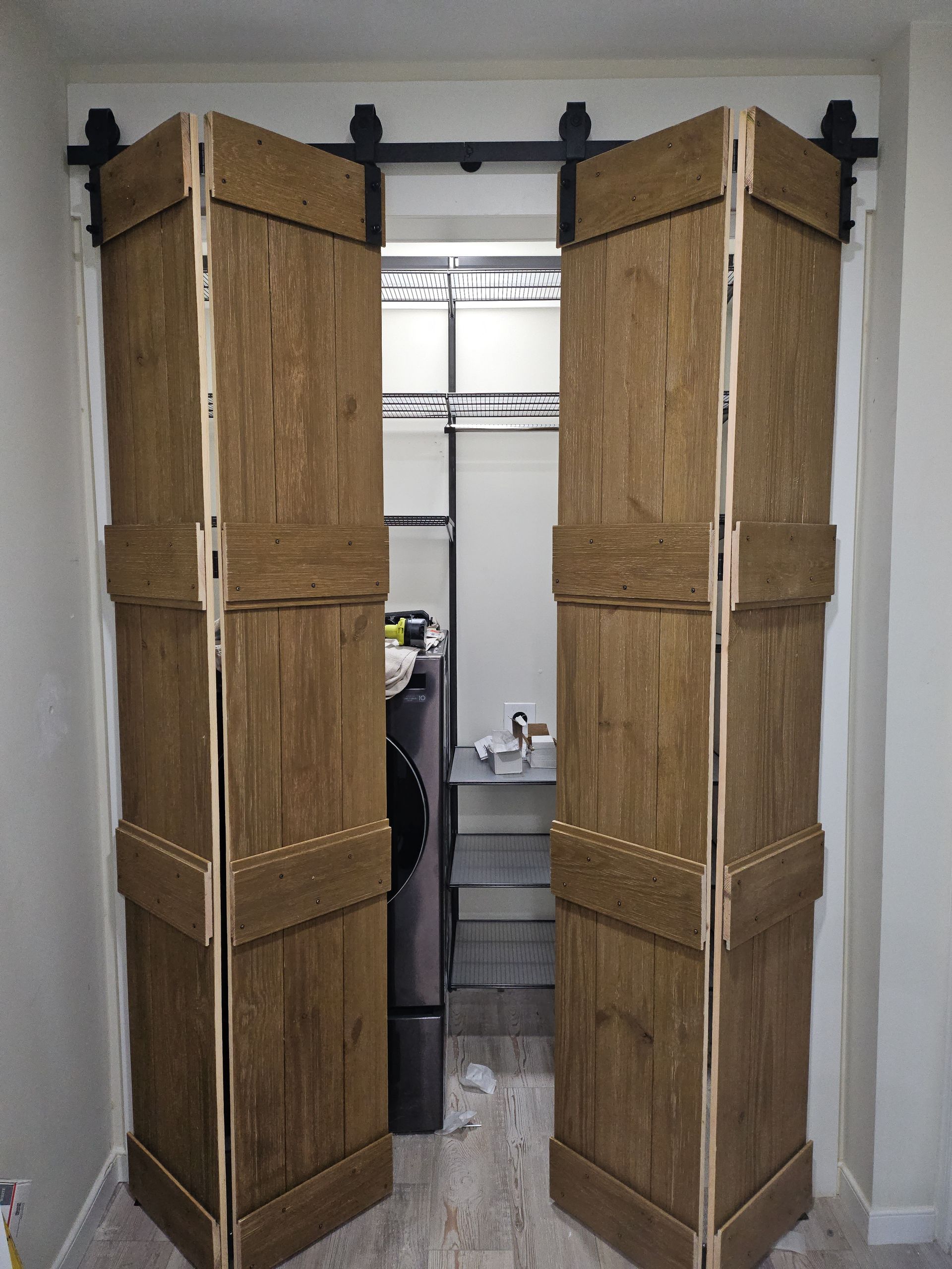 Folding barn doors, wood-toned, with black hardware, open to reveal a closet interior.