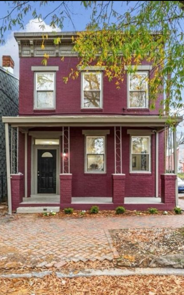 Two-story brick house with burgundy exterior and small front porch. Paver sidewalk.