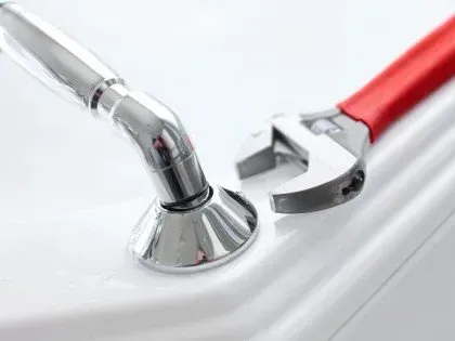 Chrome faucet handle and red-handled wrench on a sink rim