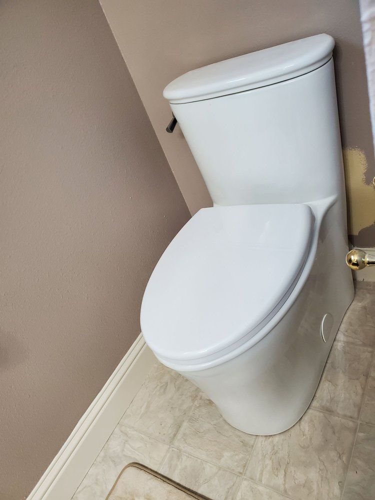 White toilet in a small beige bathroom with the lid down, next to a brass door handle.
