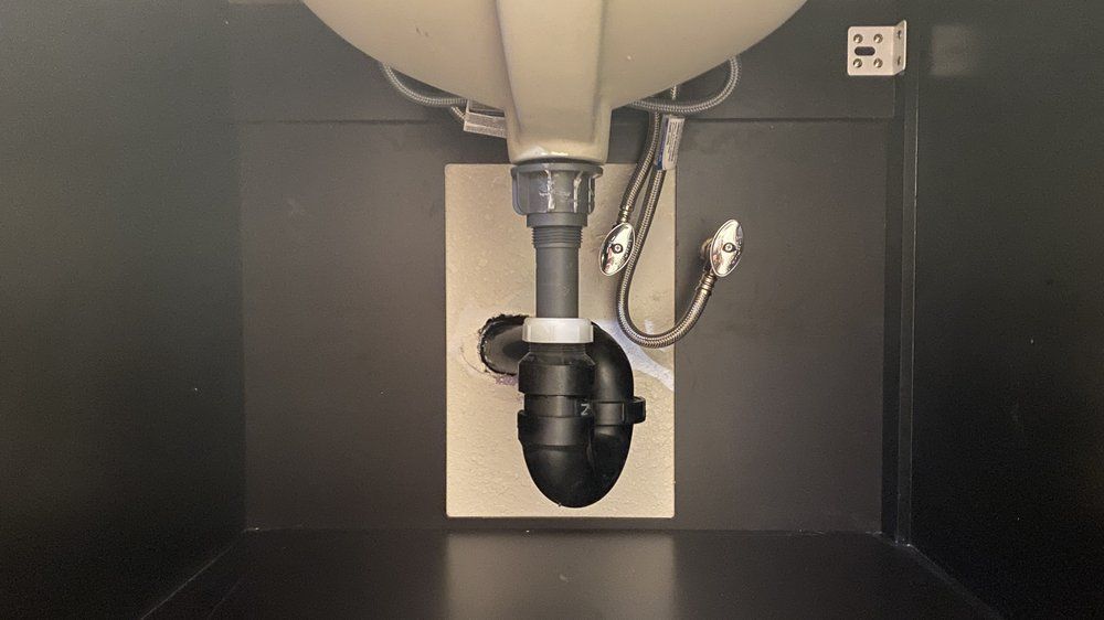 Under-sink view of a bathroom drain and black P-trap inside a cabinet.