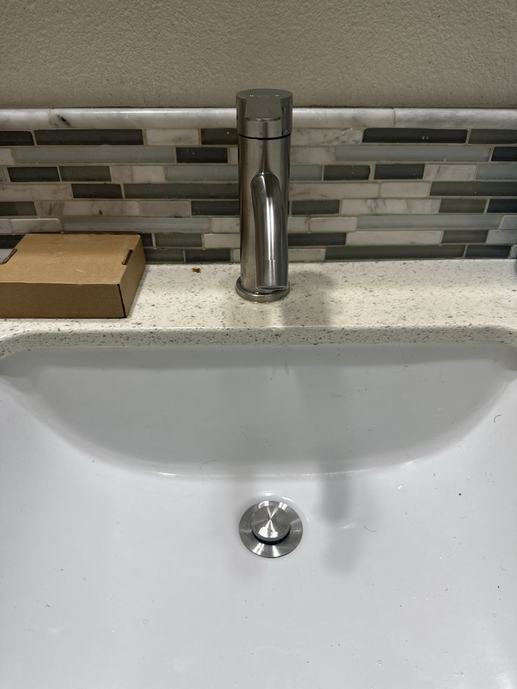 Modern bathroom sink with chrome faucet, white basin, and gray mosaic tile backsplash.