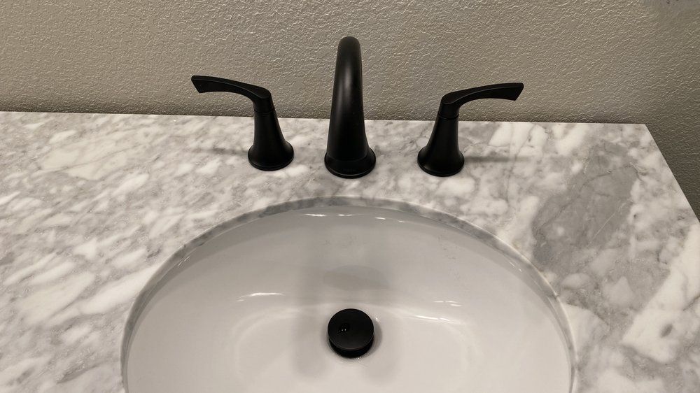 White bathroom sink with black faucet and handles on a marble countertop