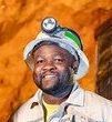 Man in mining helmet with headlamp, smiling in a mine.