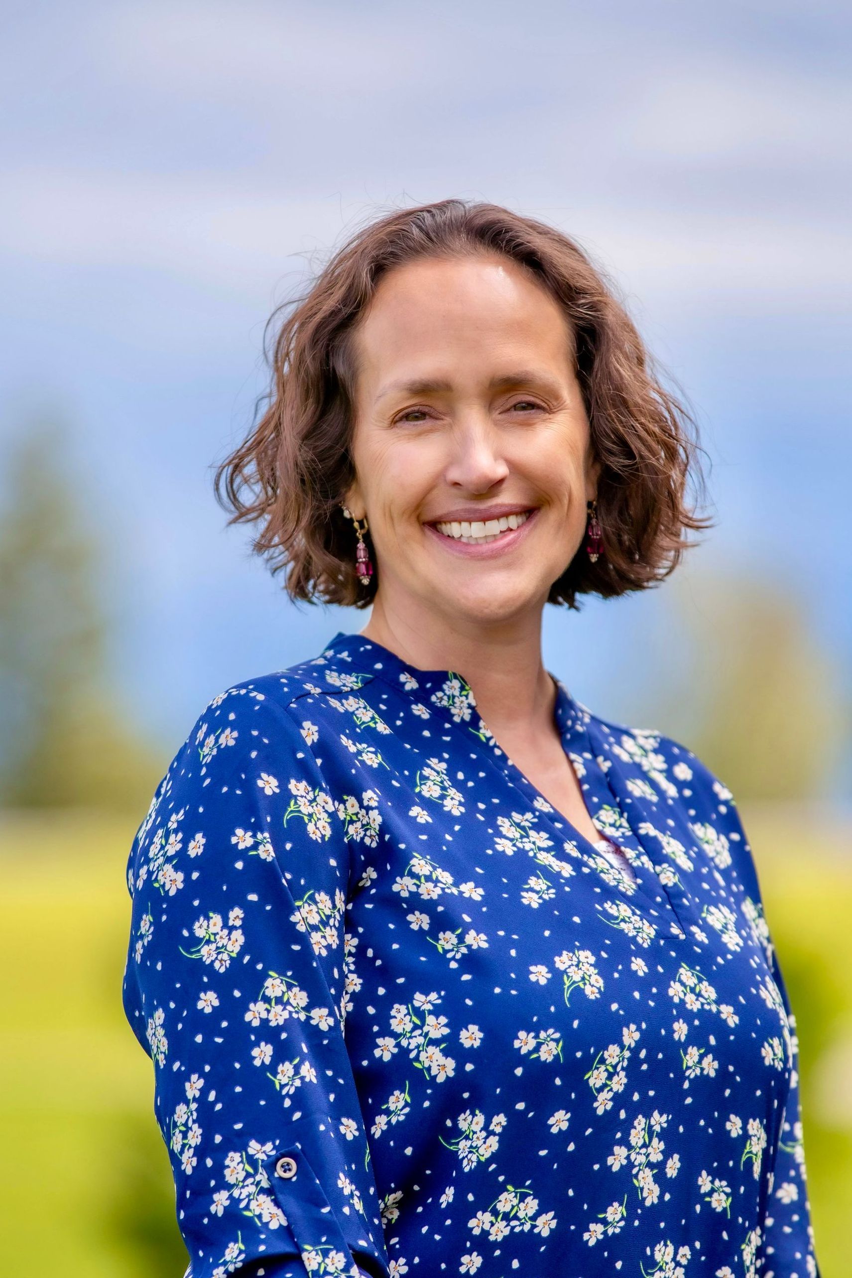 A woman in a blue floral shirt is smiling for the camera.
