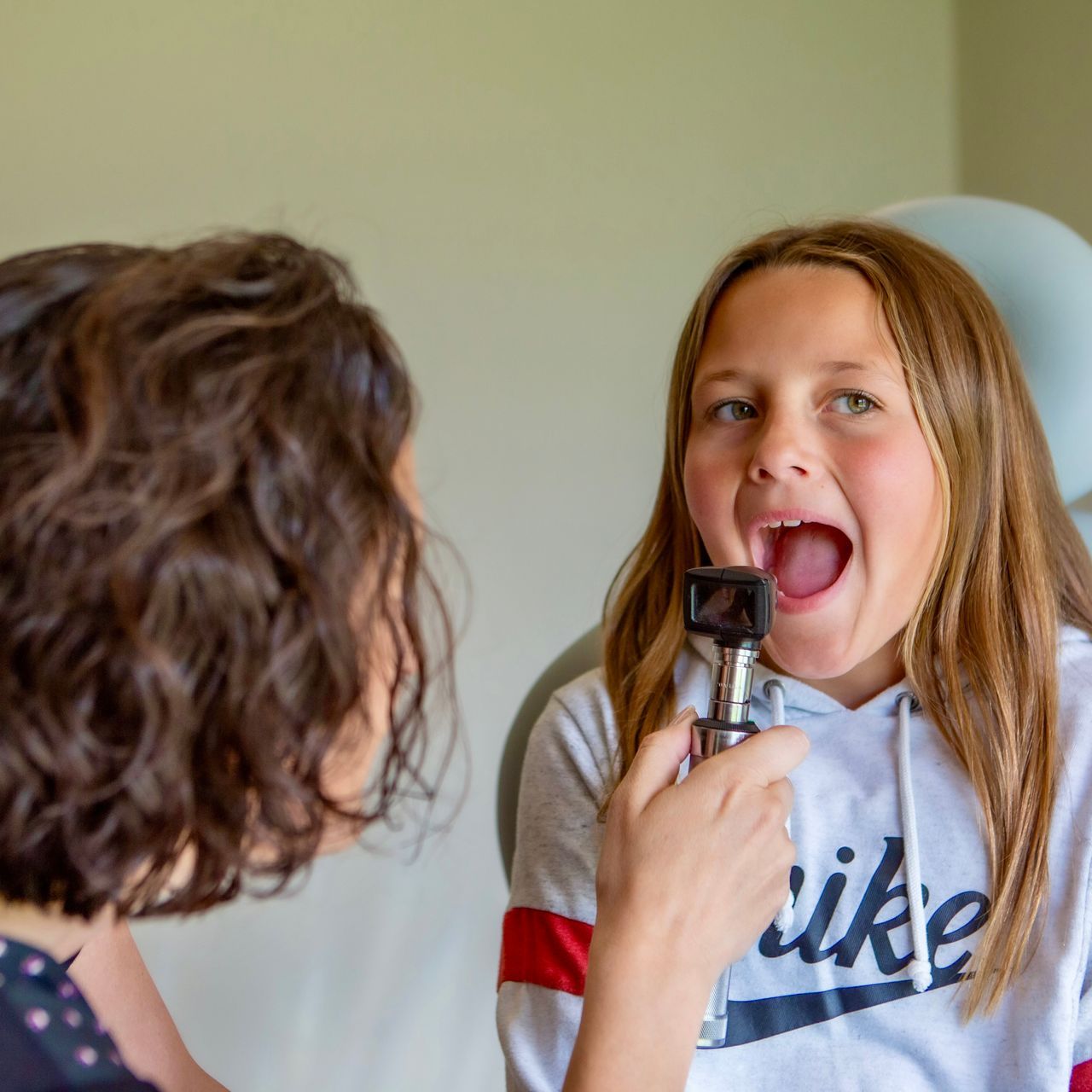 A girl wearing a nike shirt is being examined by a doctor
