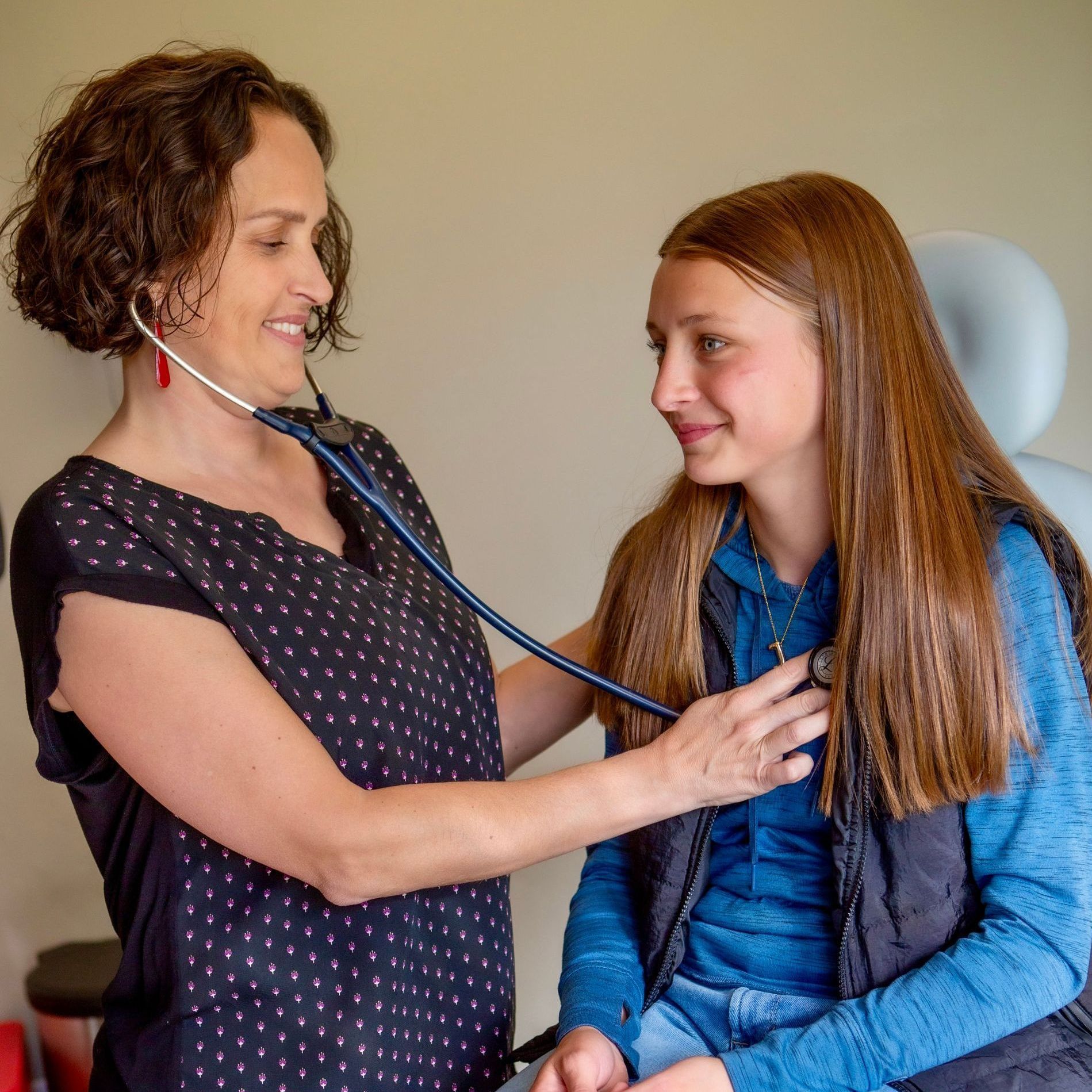 A woman is listening to a girl 's heartbeat with a stethoscope