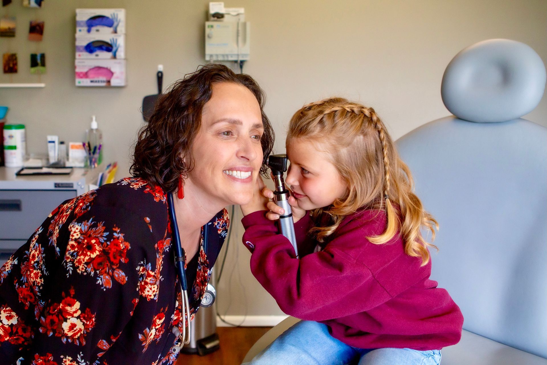 A woman is examining a little girl 's ear with an otoscope.