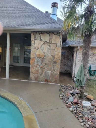 A house with a stone wall and a swimming pool in front of it.