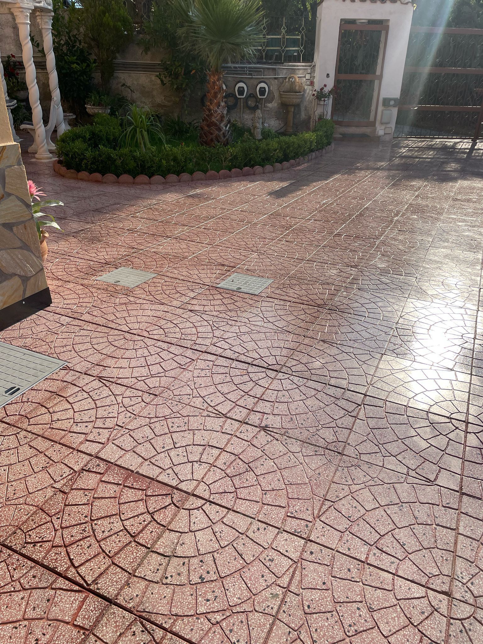 Patio pavimentato con motivi rossi e un piccolo giardino di fronte a un edificio bianco.