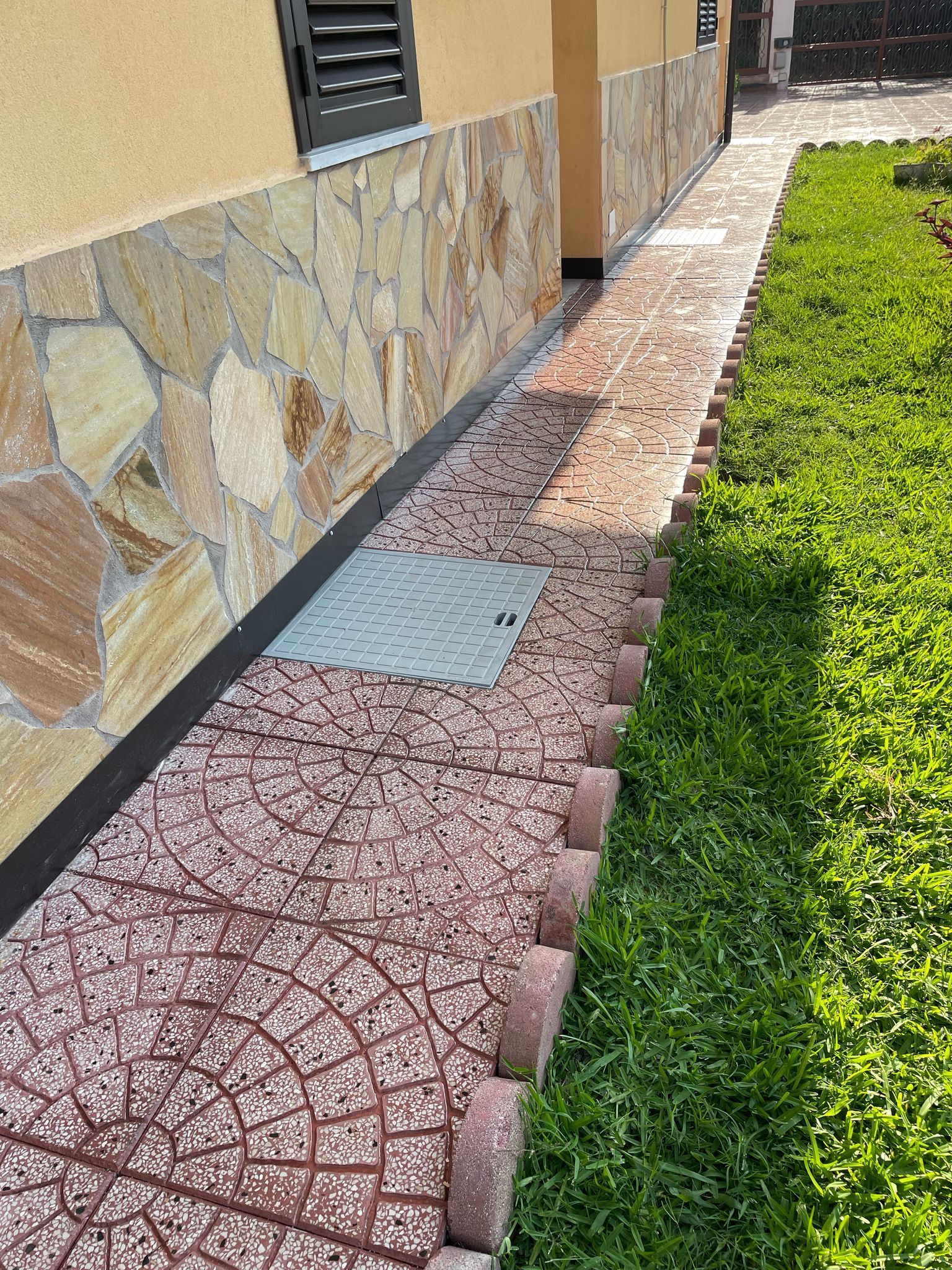 Uno stretto sentiero in pietra con un bordo in mattoni accanto a un prato verde e un muro con rivestimento in pietra.