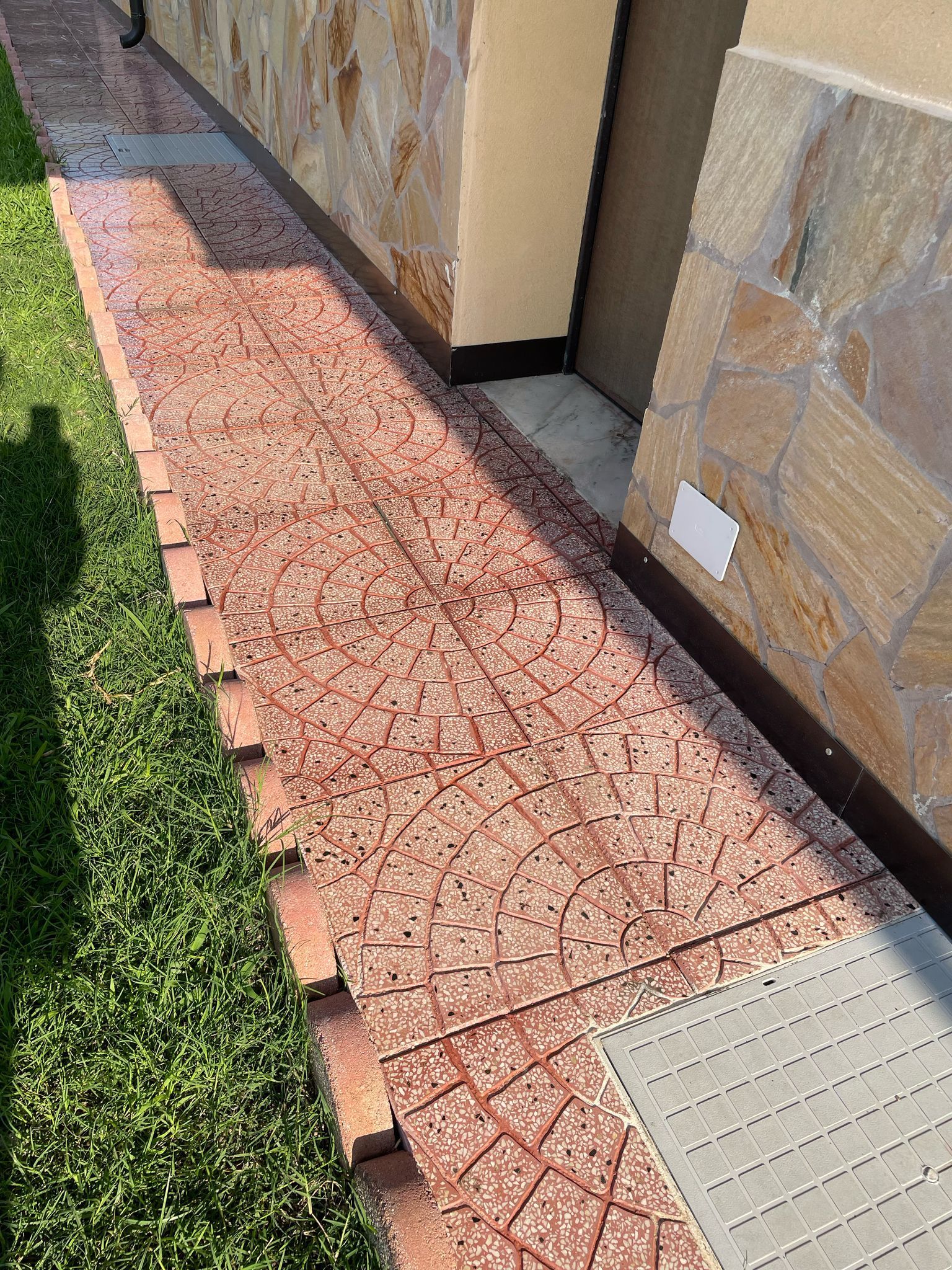 Un sentiero in mattoni con un motivo decorativo costeggia un edificio con facciata in pietra. L'erba verde costeggia il sentiero sulla sinistra.