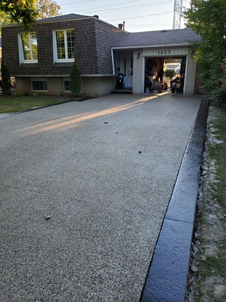 A exposed aggregate concrete driveway leading to a house with a garage.