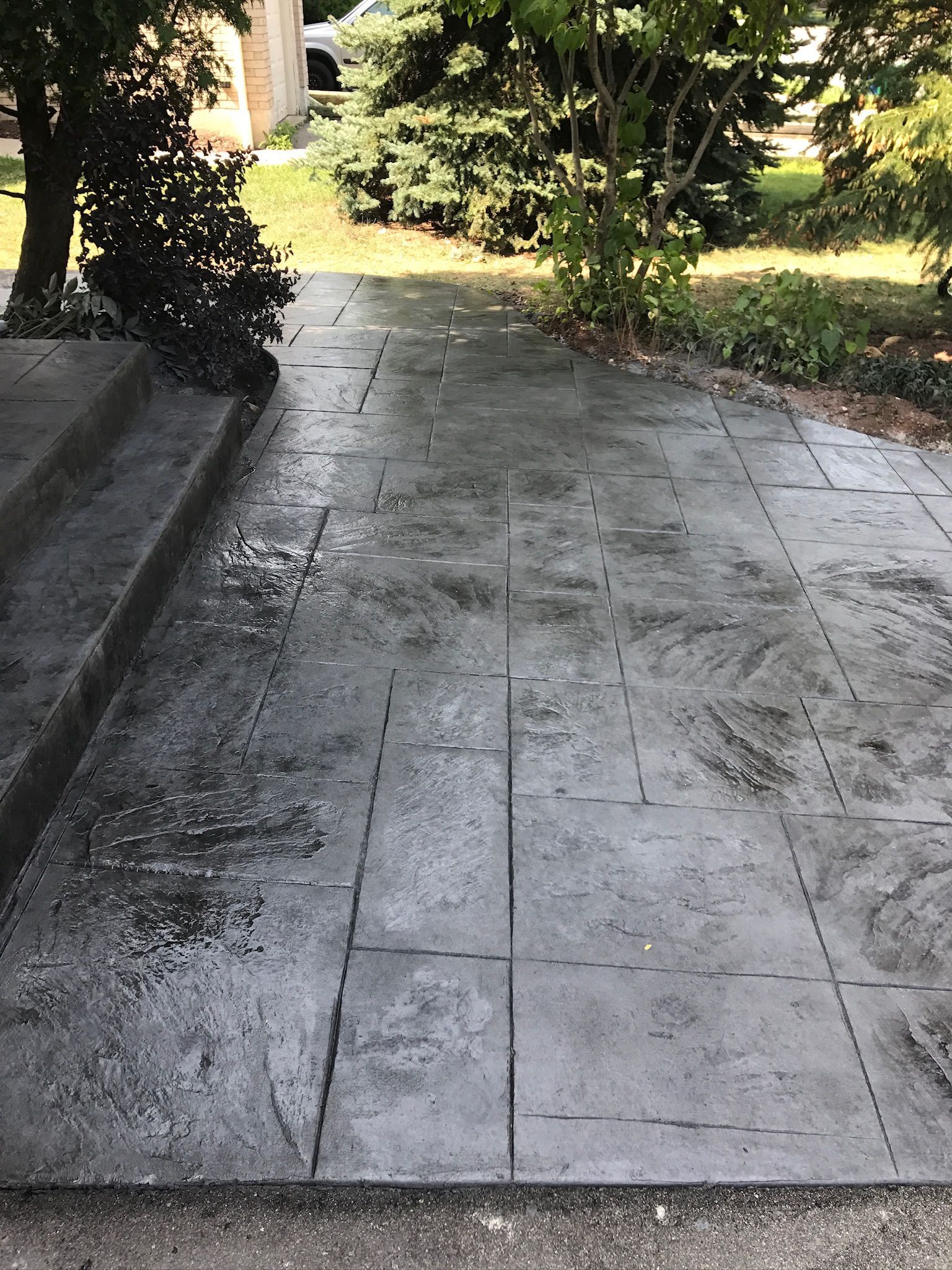 A concrete patio leading to a house with trees in the background.