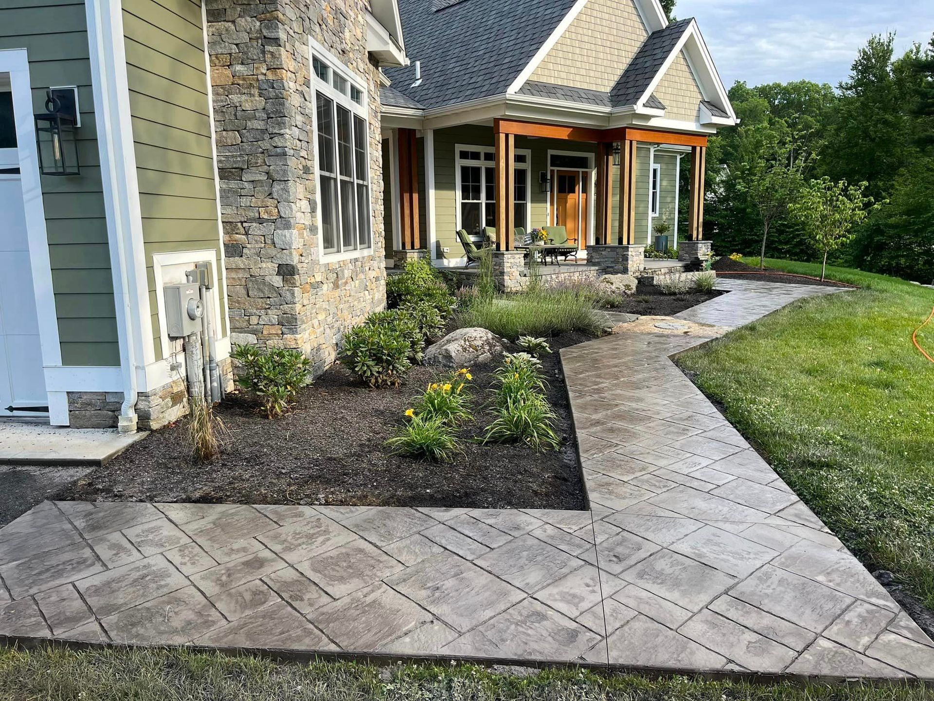 Concrete sidewalk/walkway/pathway installed with flagstone leading from front door to driveway in earth tone colours