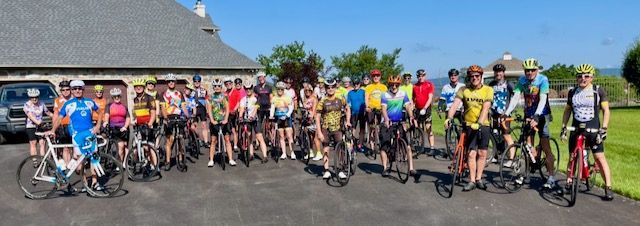 A large group of cyclists posing for a photo in front of a building on a sunny day.