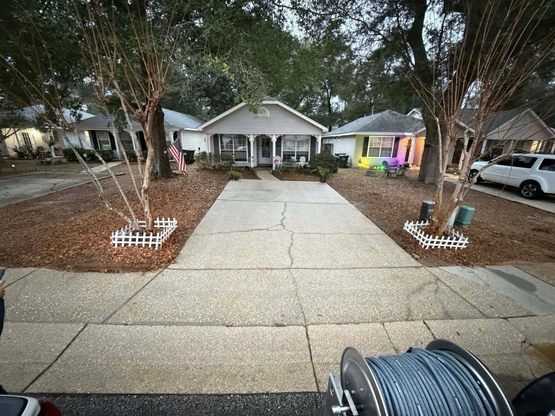 Concrete driveway freshly power washed leading to a house with trees. .