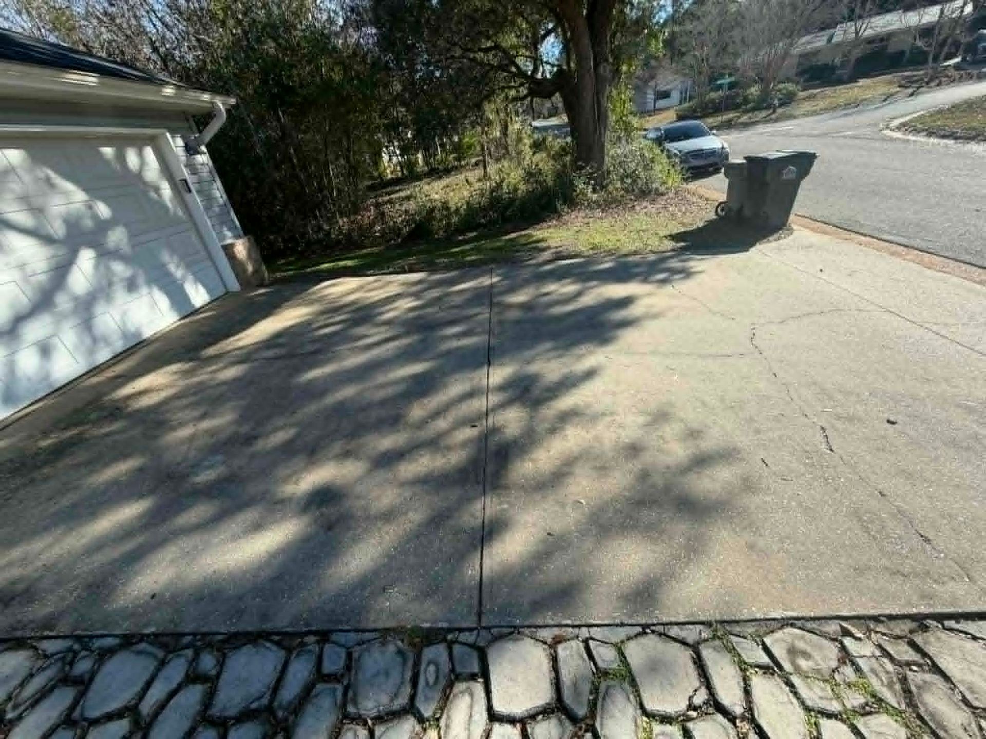 Concrete driveway with tree shadows, garage on left, stone border, and street view.