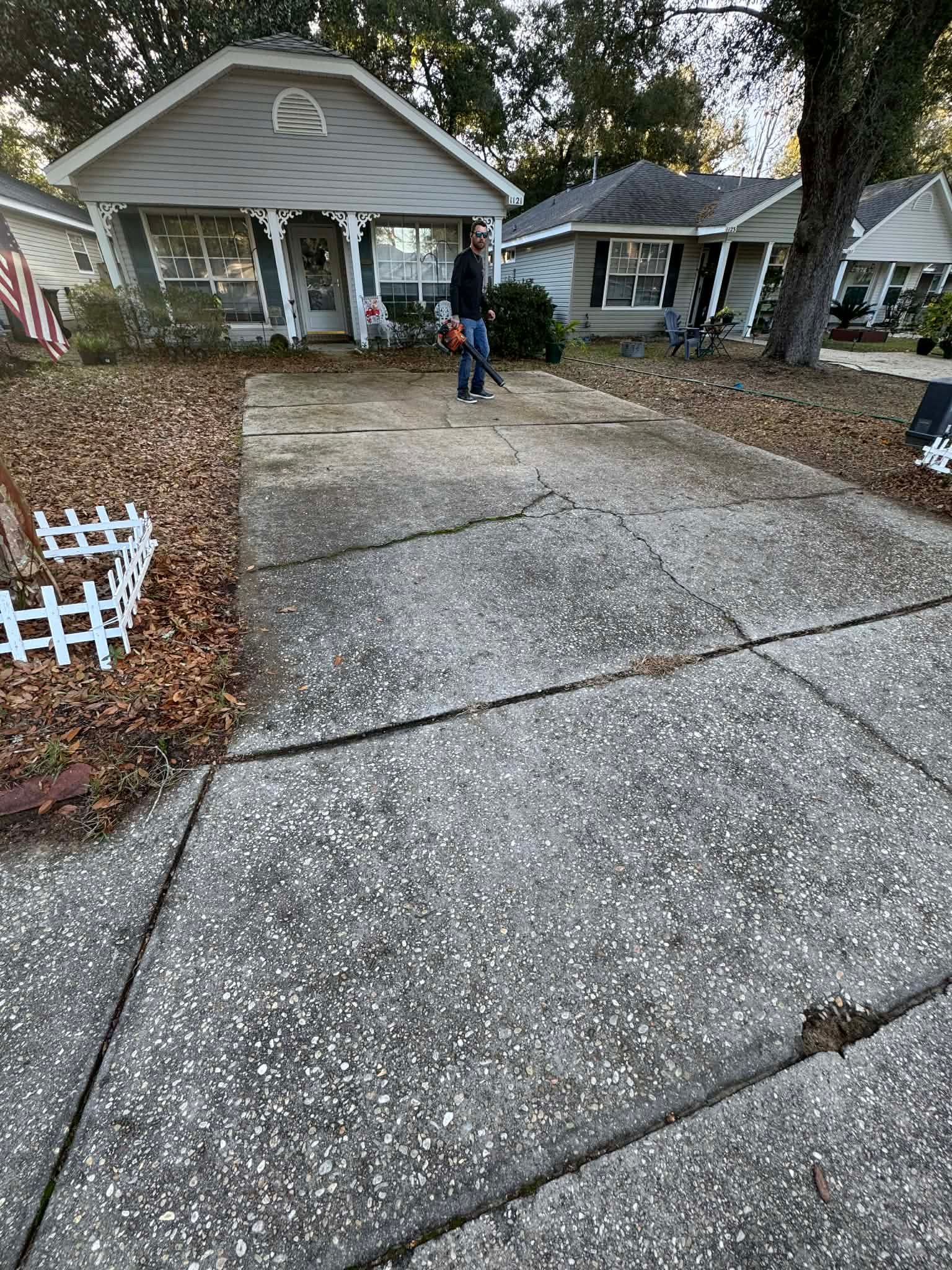 Driveway with cracks leading to houses; a person stands near the middle, prepping for power washing. 