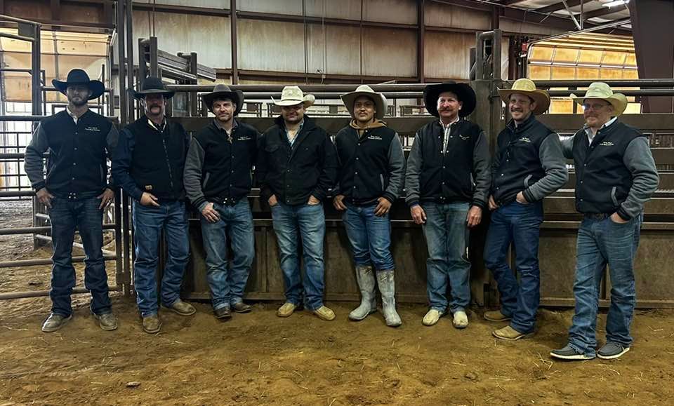 A group of cowboys are posing for a picture in a barn.