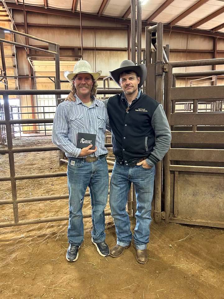 Two men in cowboy hats are standing next to each other in a rodeo arena.