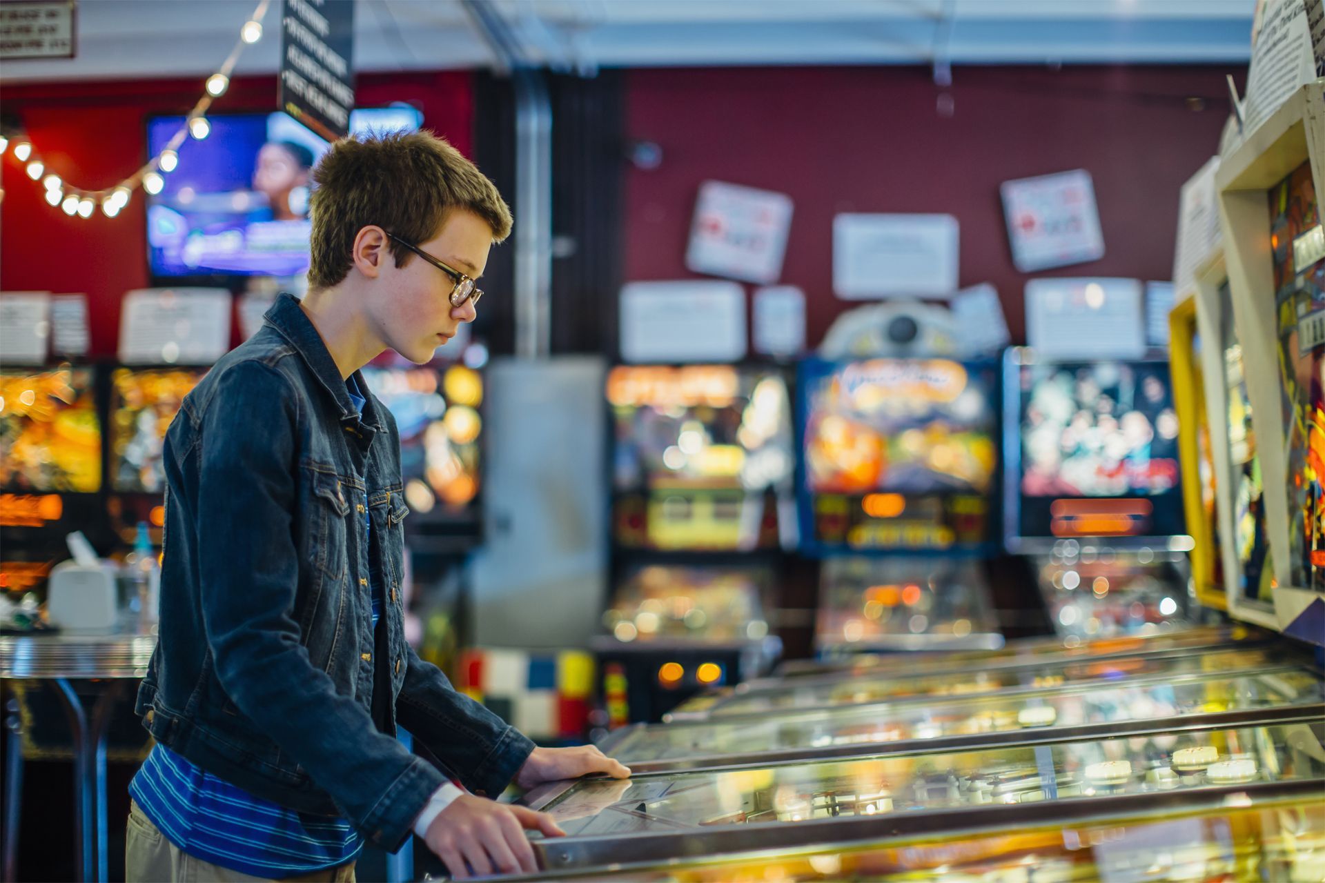 A young man is playing a pinball machine in an amusement park.