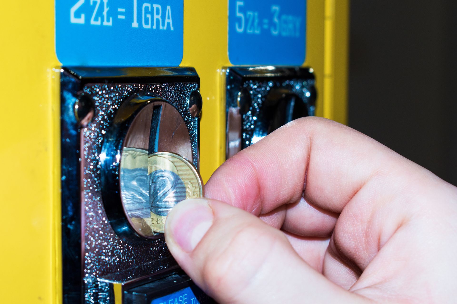 A person is putting a coin into a machine that says 2 zł = 1 gra