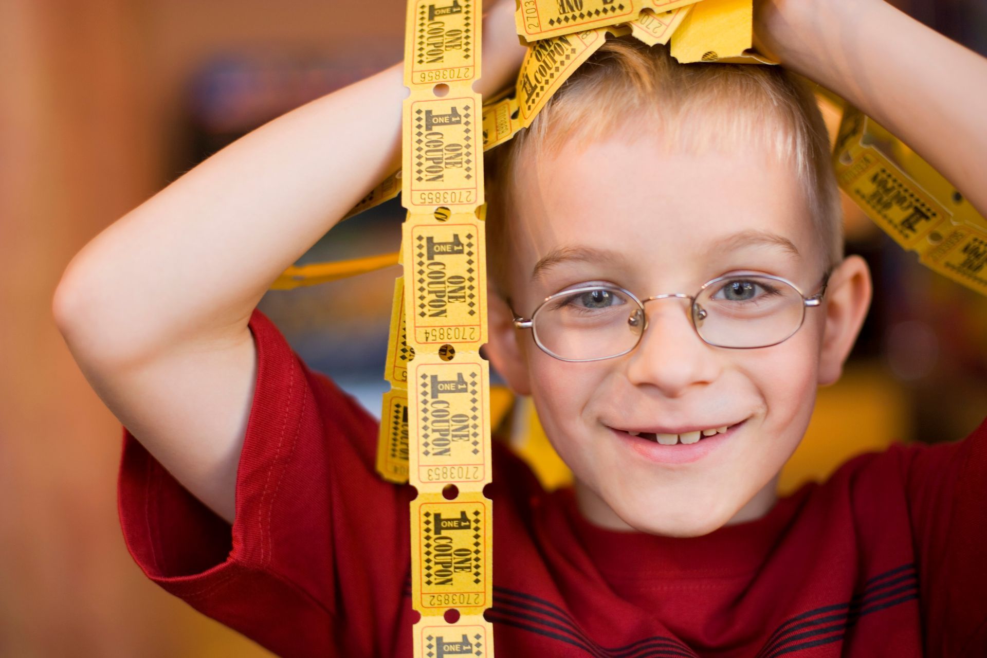 A young boy wearing glasses is holding a row of yellow tickets over his head.