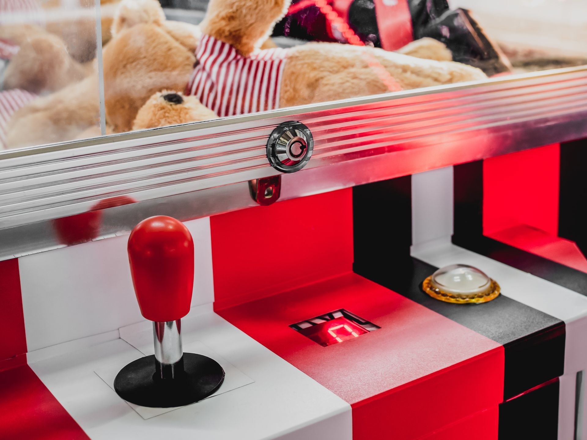 A teddy bear is sitting in a claw machine.